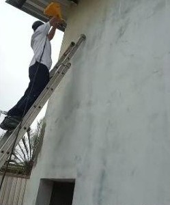 Pintor em escada pintando parede externa alta