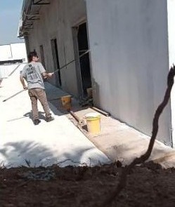 Pintor aplicando tinta com rolo em parede externa de galpão
